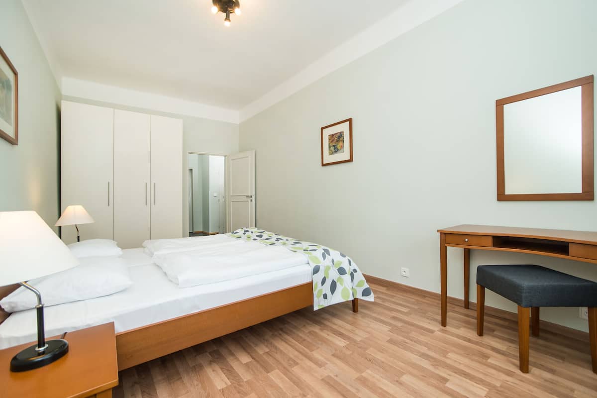 Quarto de hotel com cama, escrivaninha, cadeira, guarda-roupa e espelho.
