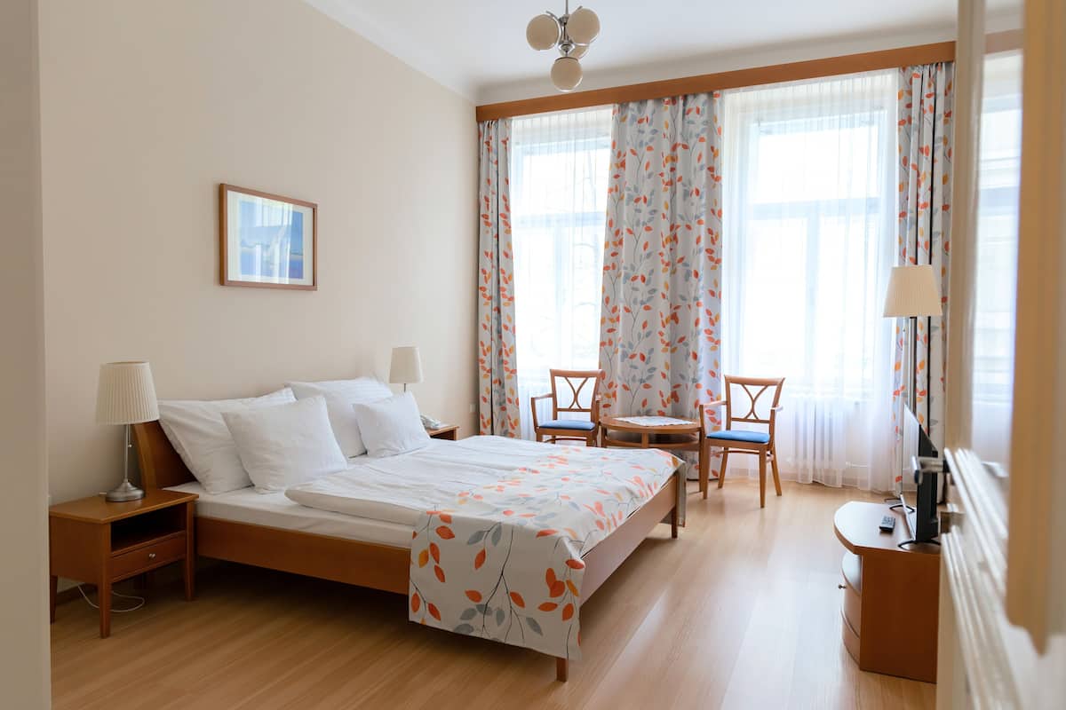 Quarto de hotel com cama, mesas de cabeceira, escrivaninha com cadeira, luminária e um quadro na parede.