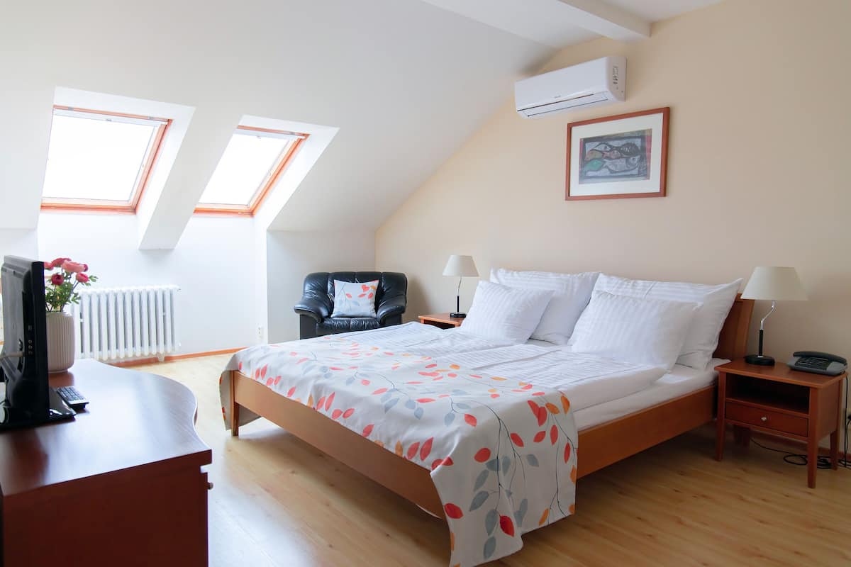 Quarto com cama, escrivaninha, cadeira, duas janelas, ar-condicionado e um quadro na parede.