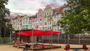 Ein Spielplatz mit rotem Baldachin, Sand und einer Rutsche.