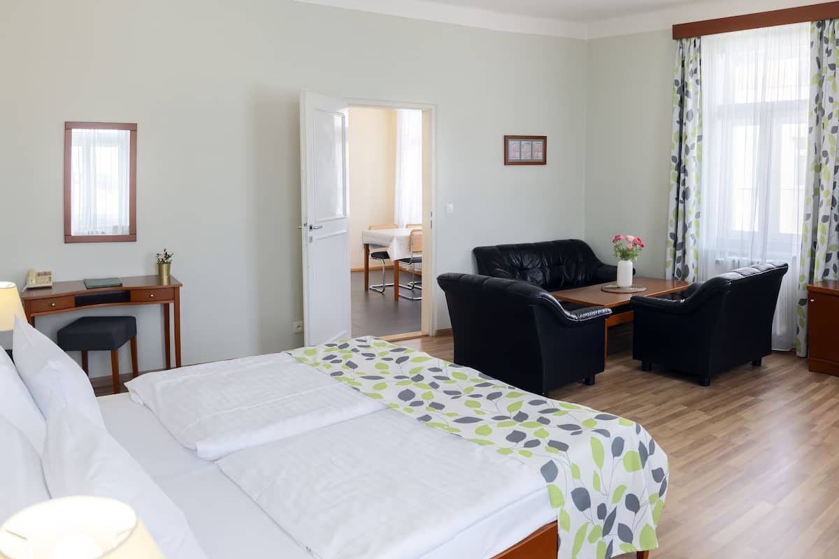 Quarto de hotel com cama, escrivaninha, cadeira, televisão e área de refeições.