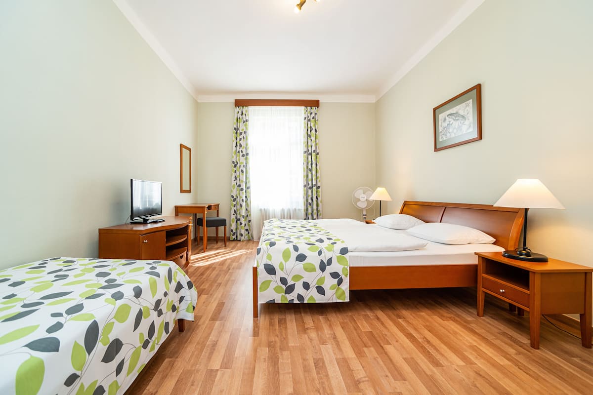 Quarto de hotel com duas camas, uma escrivaninha, televisão e janela com cortinas.