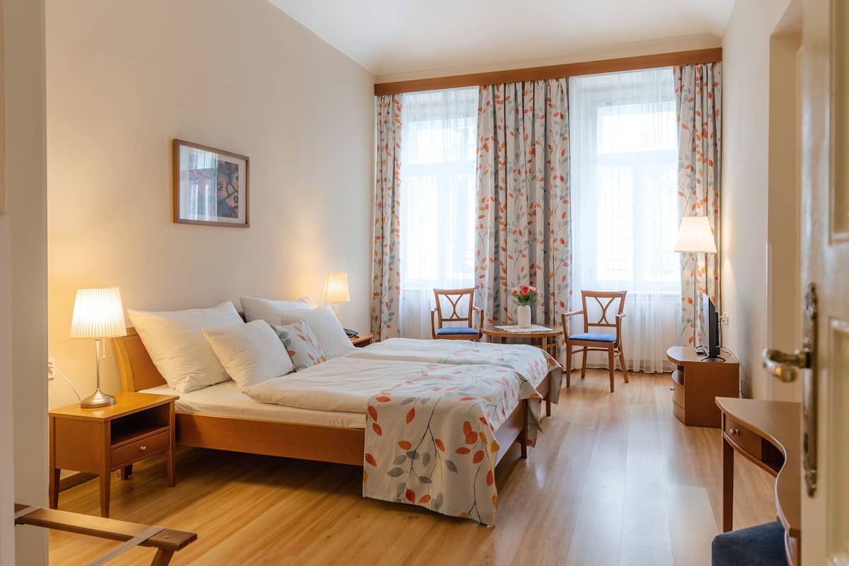 Quarto de hotel com cama, mesas de cabeceira, escrivaninha e uma cadeira.