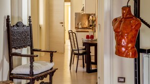 Una habitación con una silla de madera, una mesa de comedor con sillas, una zona de cocina y un maniquí.