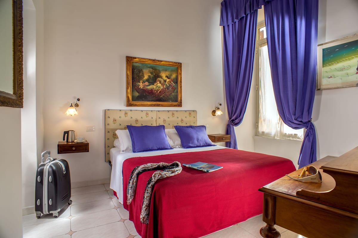 Une chambre d’hôtel avec un lit, un bureau, une valise et un tableau accroché au mur.
