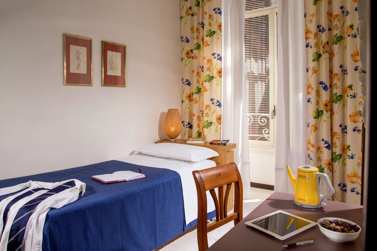 Une chambre d’hôtel avec un lit, une chaise, une table avec une bouilloire, un bol et une tablette.
