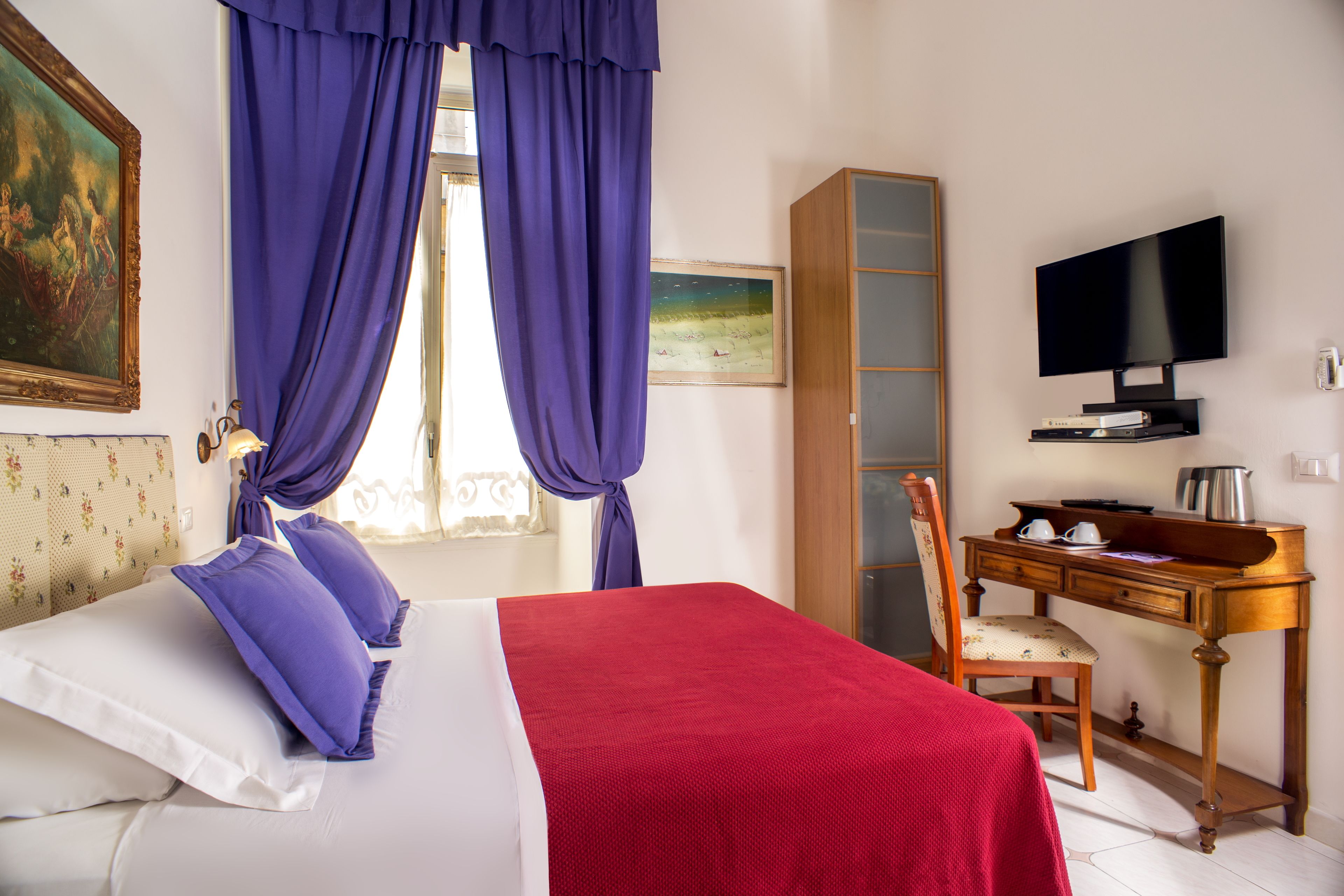 A hotel room with a bed, a desk, a television, and a window with curtains.