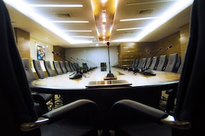 A conference room with a long table, multiple microphones, and chairs arranged around it.