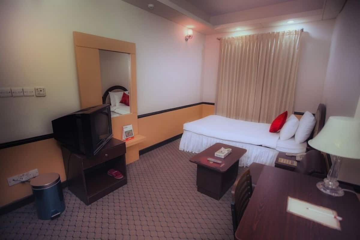 A hotel room with a bed, a television, a small table, a lamp, and a mirror.