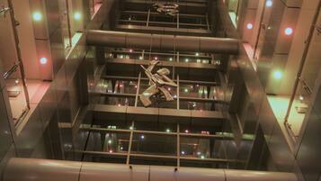 A modern interior with a central escalator surrounded by reflective surfaces and illuminated by colorful lights.