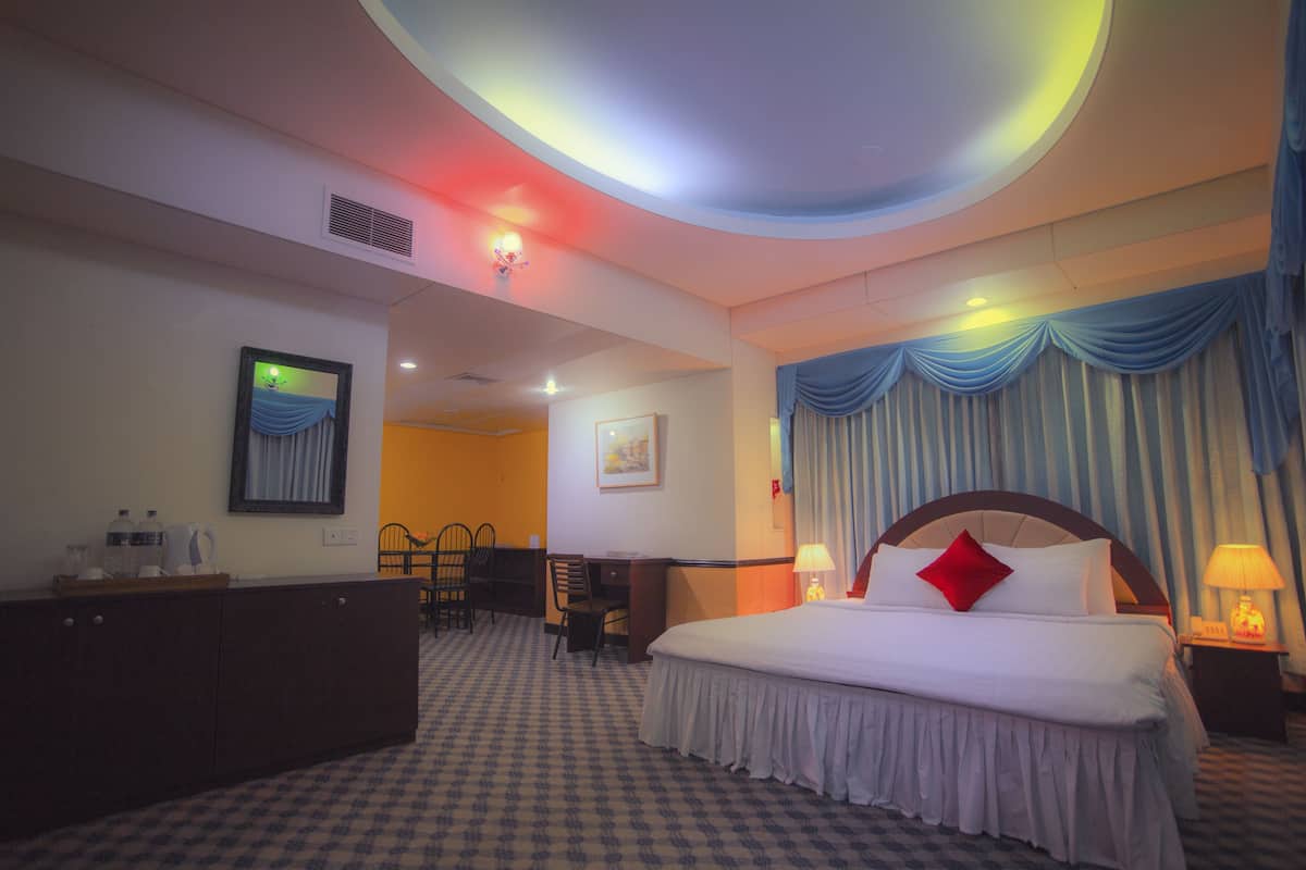 A hotel room with a large bed, a desk, a chair, and a wardrobe.