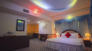 A hotel room with a large bed, a desk, a chair, and a wardrobe.