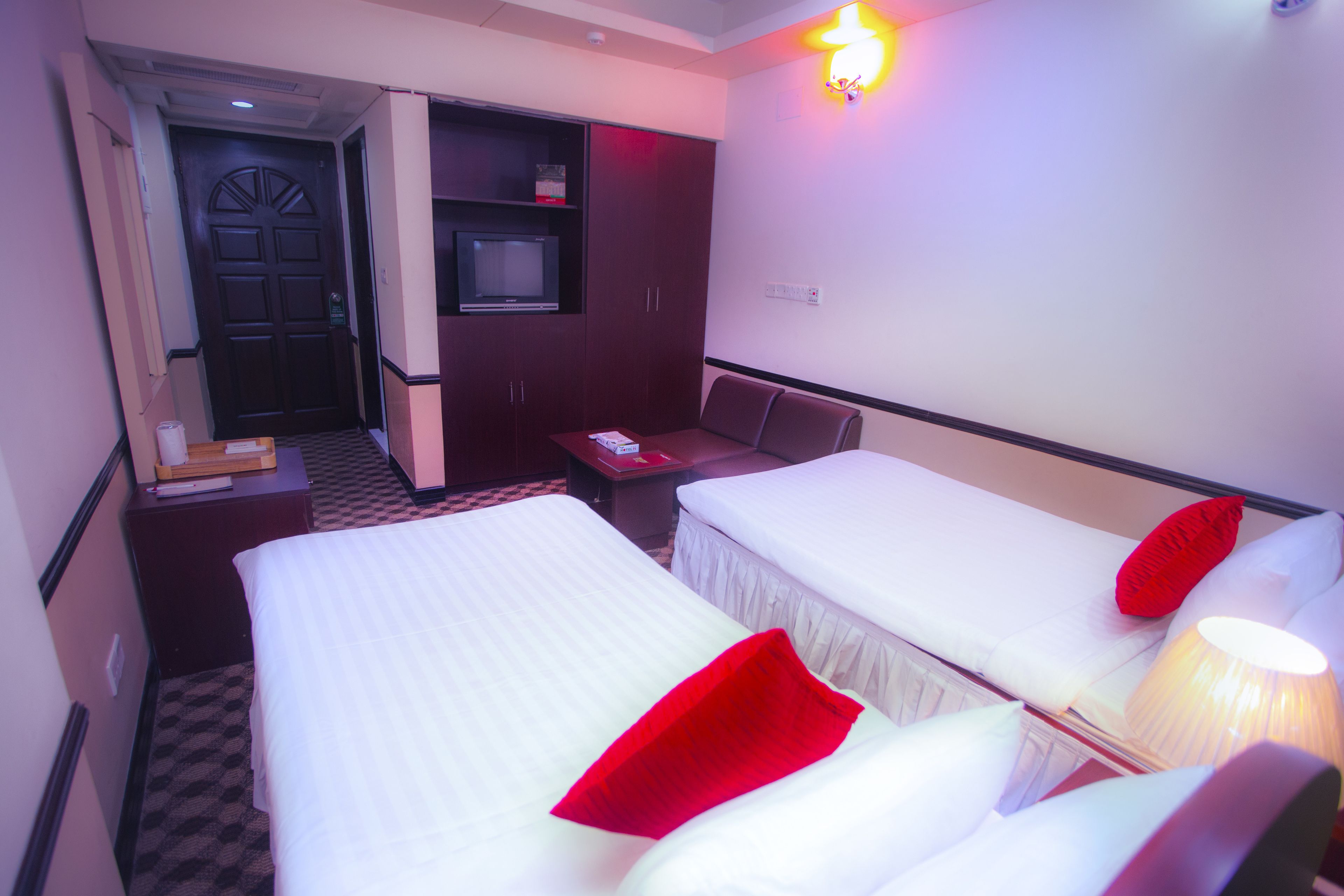 Habitación de hotel con dos camas, un televisor, un escritorio y una almohada roja.