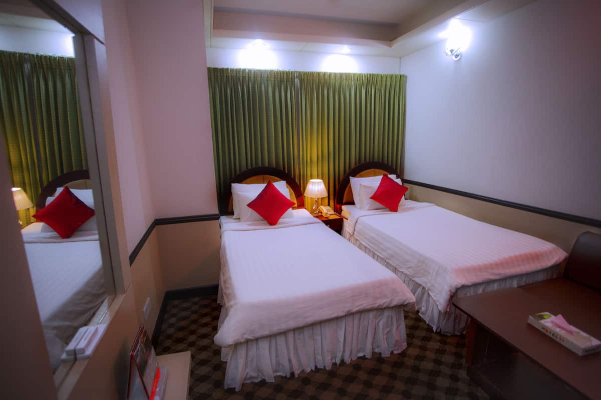 A hotel room with two single beds, a desk, a chair, a mirror, and a window with curtains.