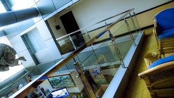A high-ceilinged lobby with a glass railing, a reception desk, and a blue cushioned chair.