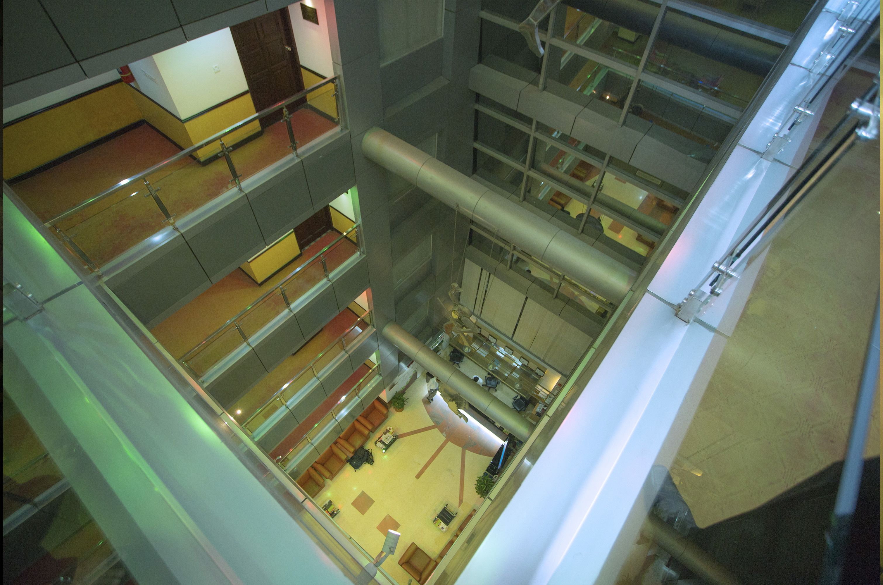 Un atrium à plusieurs niveaux, doté de rampes en verre, de nombreux étages et d’un espace central ouvert aménagé avec des sièges et des plantes.