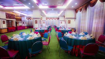 A banquet hall with multiple round tables, each set with white tablecloths, blue chairs, and neatly arranged table settings.