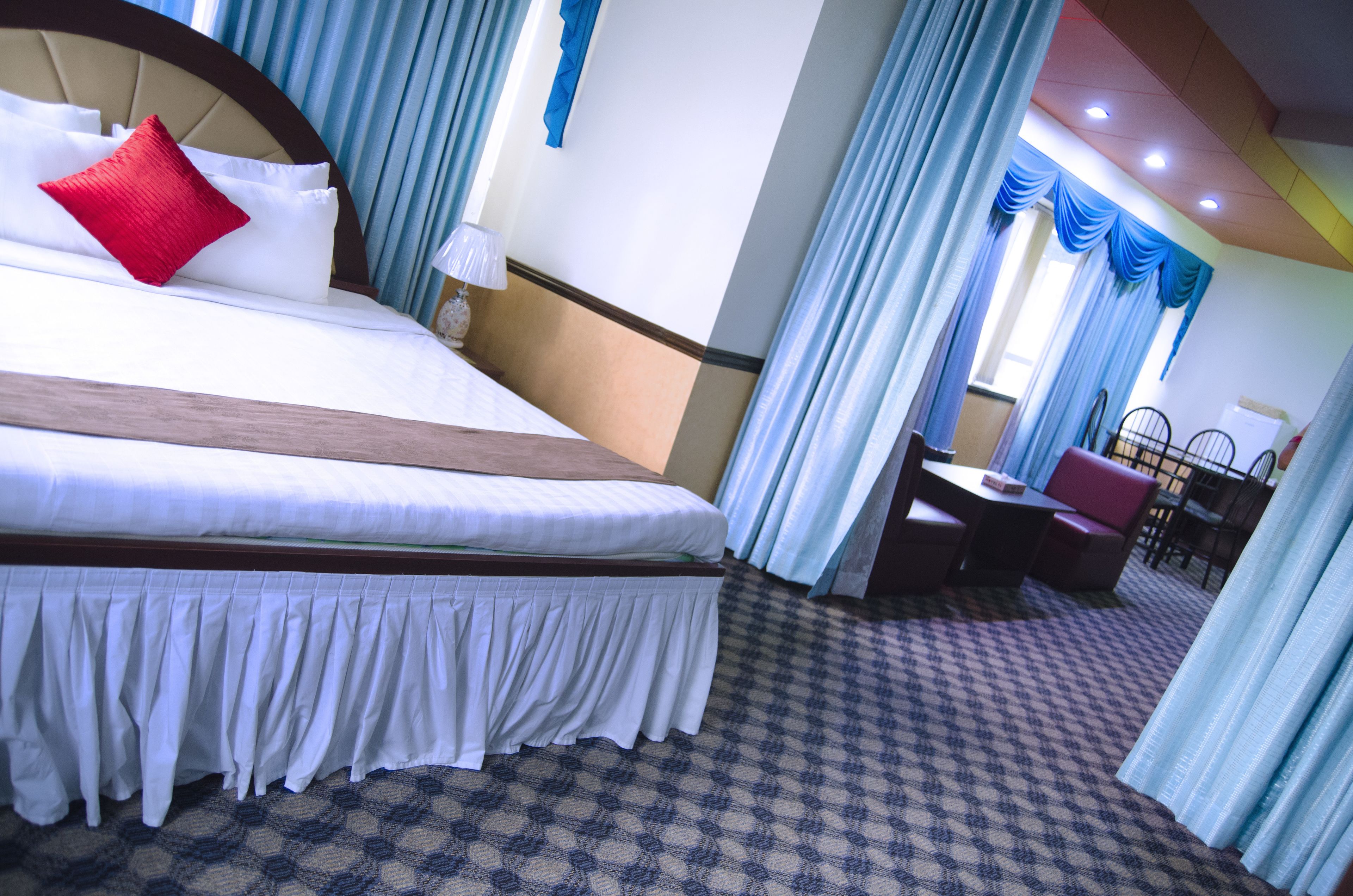 A hotel room with a large bed, a dining area, and a view of the outside.