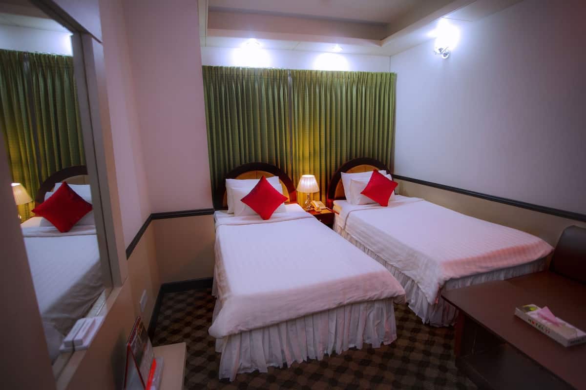 A hotel room with two beds, a desk, a mirror, and a window with curtains.