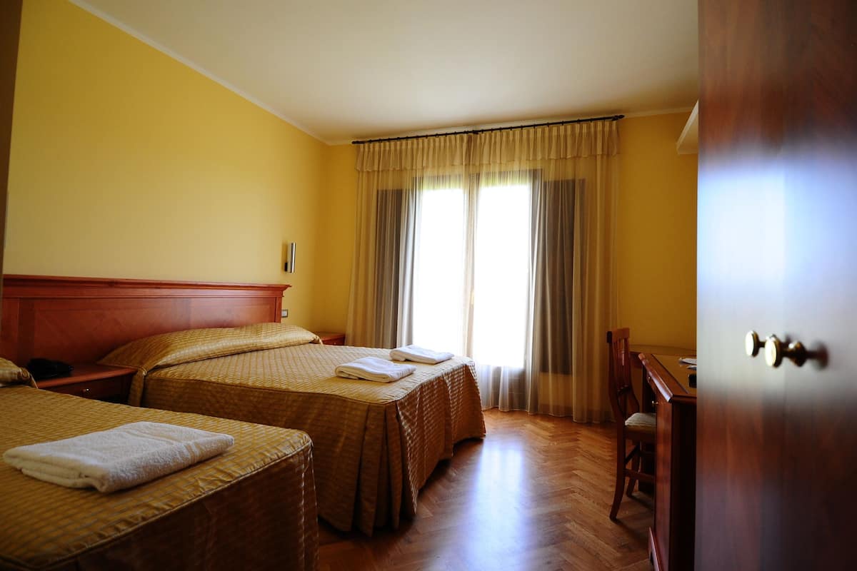 Ein Hotelzimmer mit zwei Betten, einem Holzkopfende, einem Schreibtisch und einem Fenster mit Vorhängen.