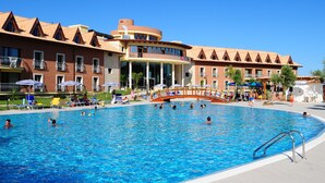 Una piscina con un puente, rodeada por un hotel con varios balcones y un cielo azul despejado.