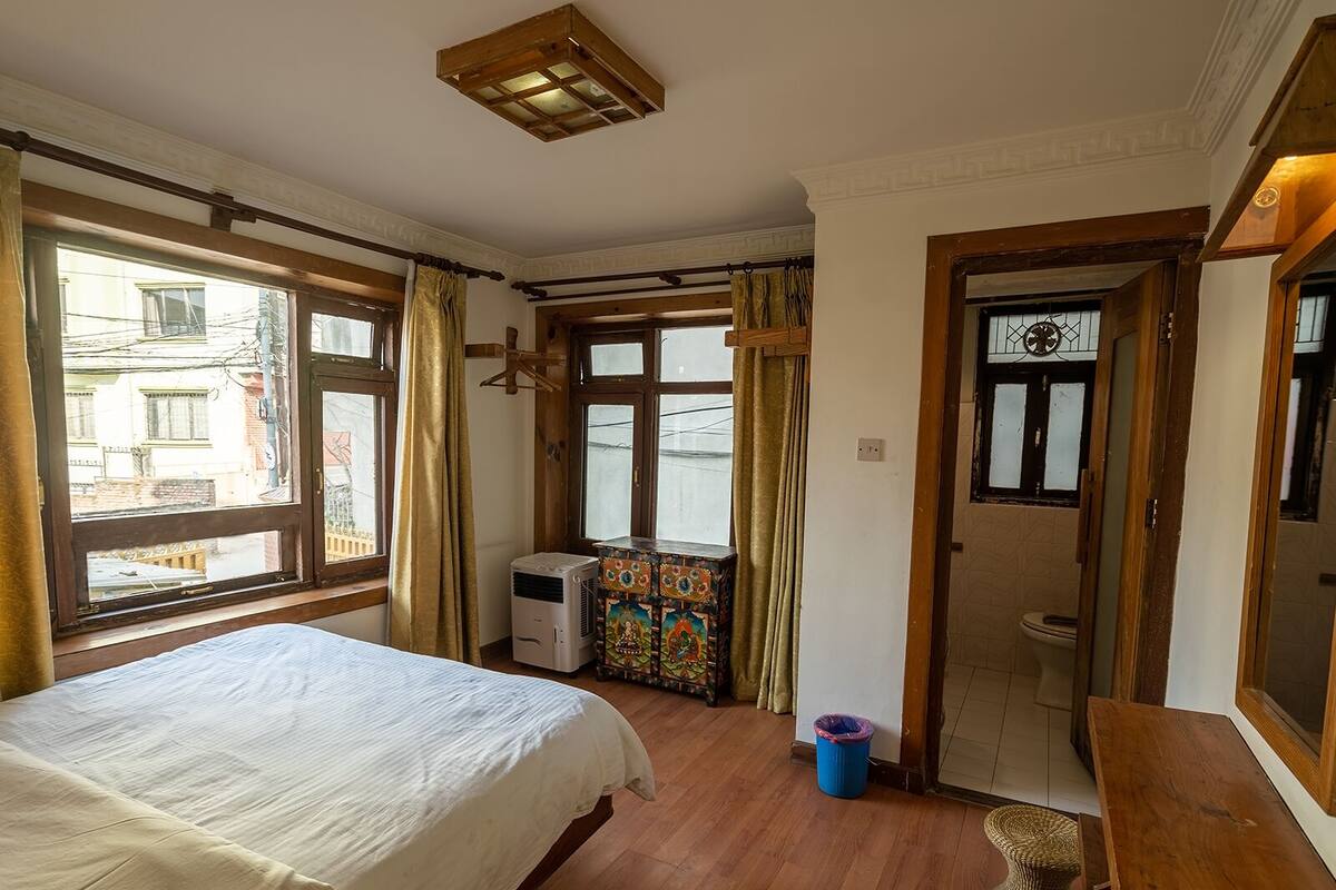 A bedroom with a bed, a window, a heater, a door, and a small table.