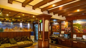 A lobby with a wooden reception desk, a sofa, and a large mural depicting a mountainous landscape. - Hotel Ganesh Himal (Kathmandu)