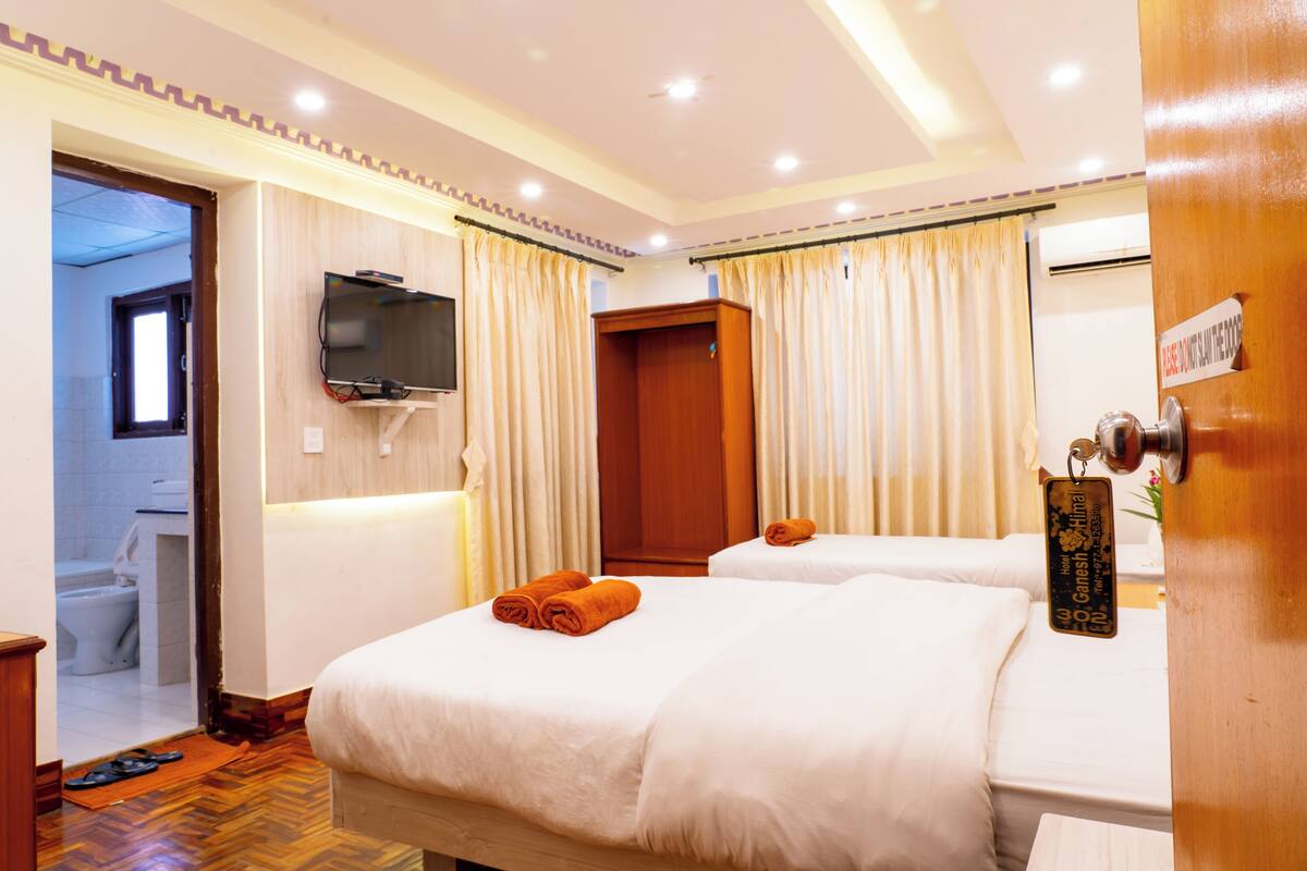 A hotel room with two beds, a television, and a wooden wardrobe.