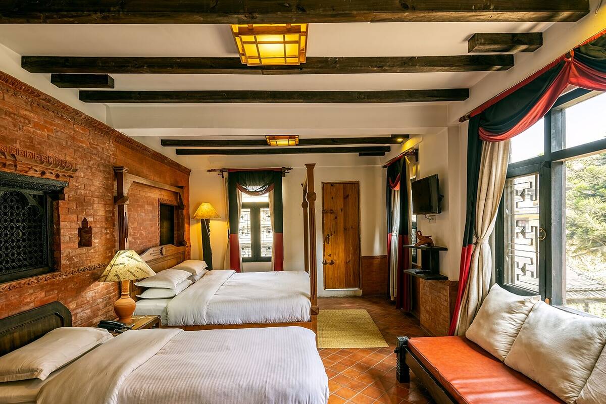 A traditional room with two beds, a wooden bench, a TV, and a brick wall.