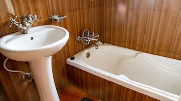 A bathroom with a white pedestal sink, a bathtub, and wooden paneling on the walls.