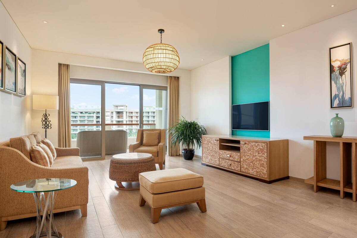 Een moderne woonkamer met een bank, voetenbankje, rond tafel en een televisie op een houten kast.
