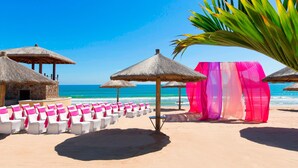 A beach with thatched umbrellas, white lounge chairs with pink sashes, and a clear blue sky. - Sheraton Sanya Haitang Bay Resort (Sanya)