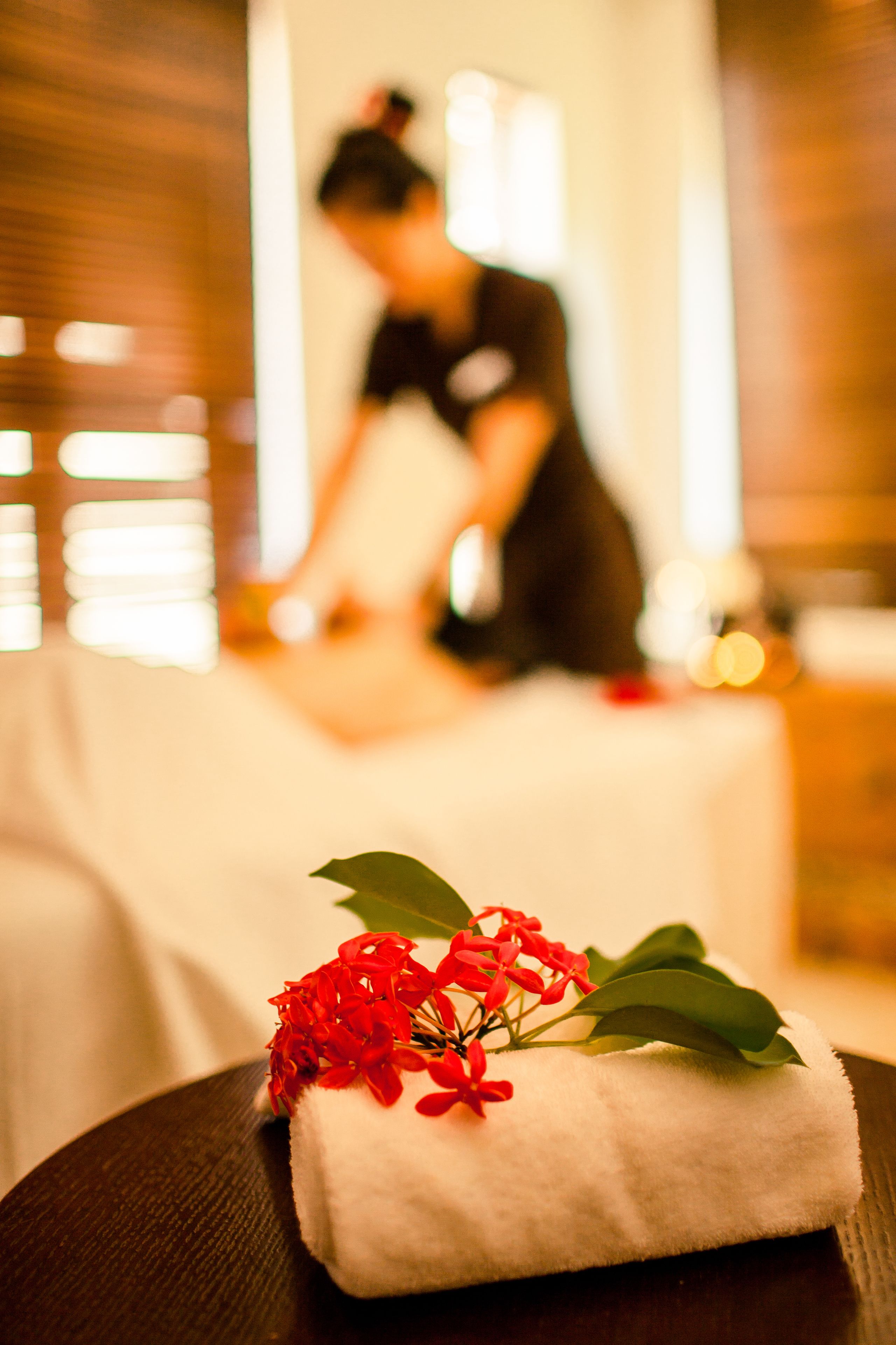 A spa setting with a massage table, a towel with red flowers, and a person in the background.