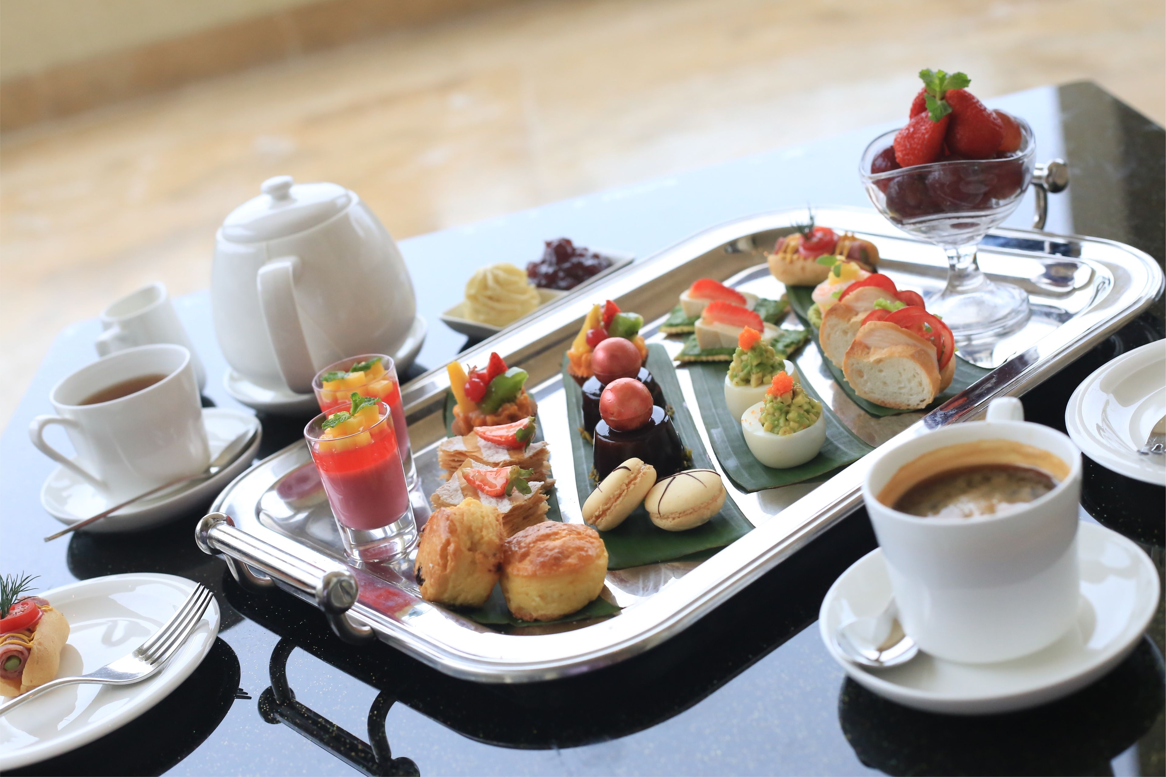 Bandeja de desayuno con diversos pasteles, frutas y bebidas sobre una mesa.