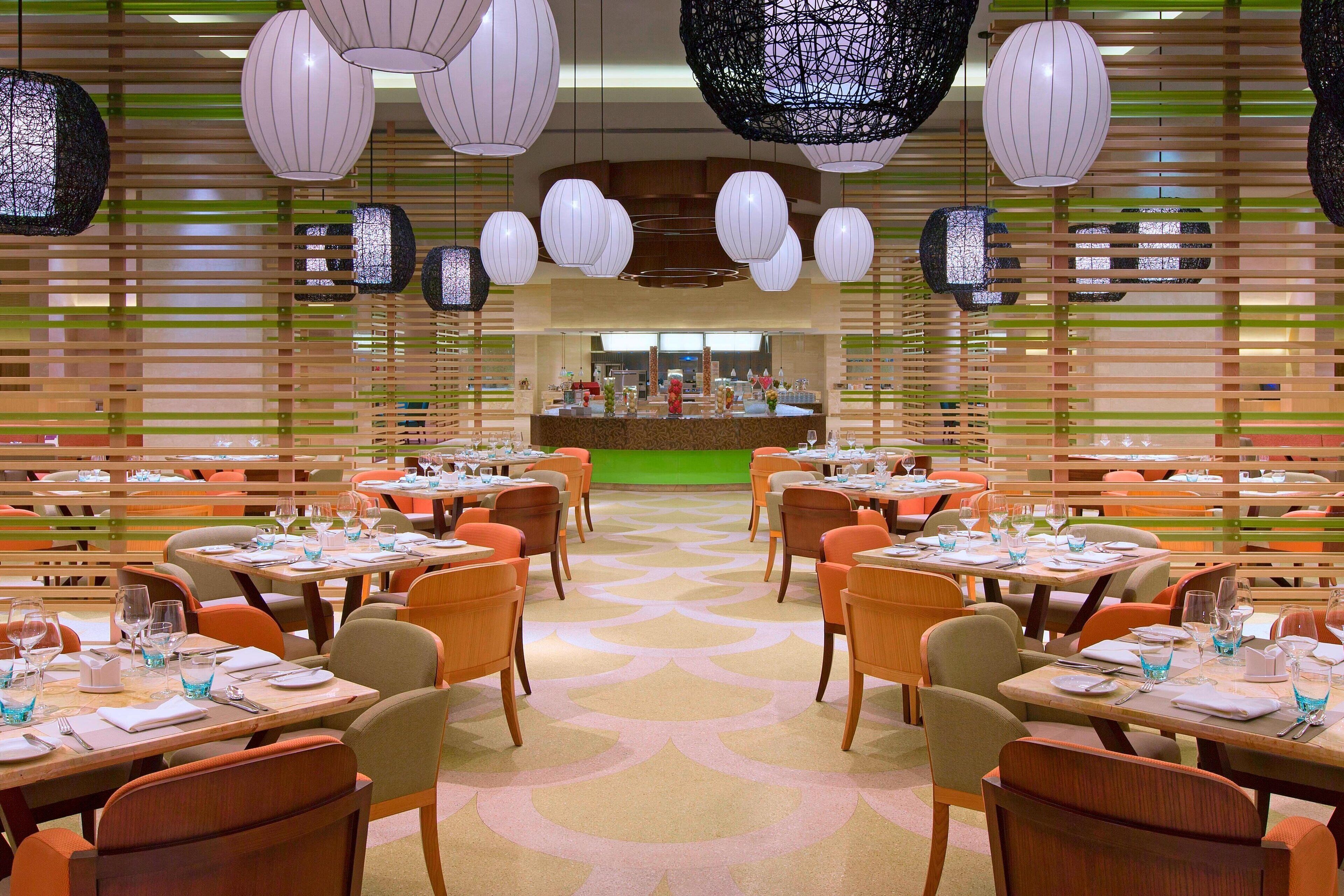 Un restaurant doté de nombreuses tables et chaises, d’un comptoir central et de luminaires sphériques suspendus.