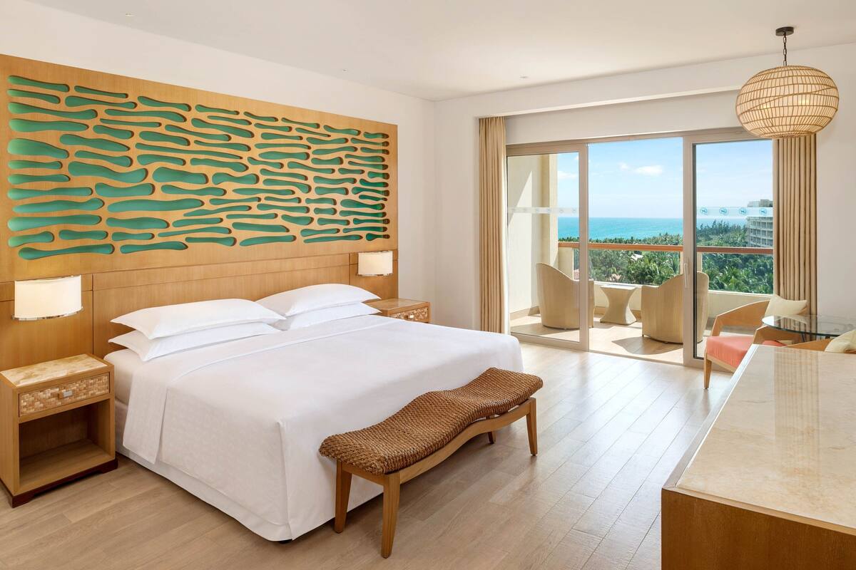 Een moderne hotelkamer met een groot bed, een houten hoofdeinde en uitzicht op zee.