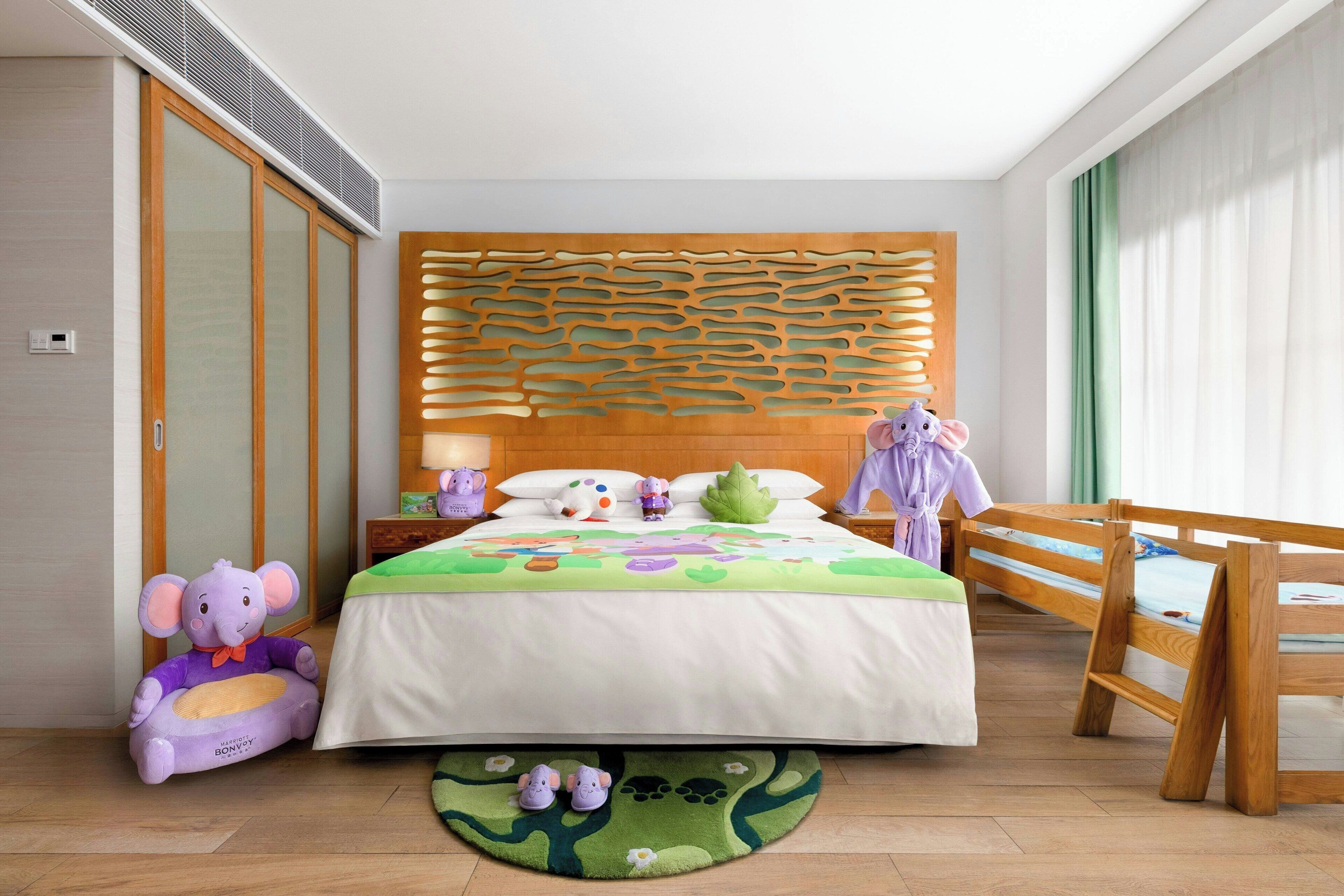 A bedroom with a bed, a wooden headboard, a nightstand, a purple elephant toy, and a green rug.