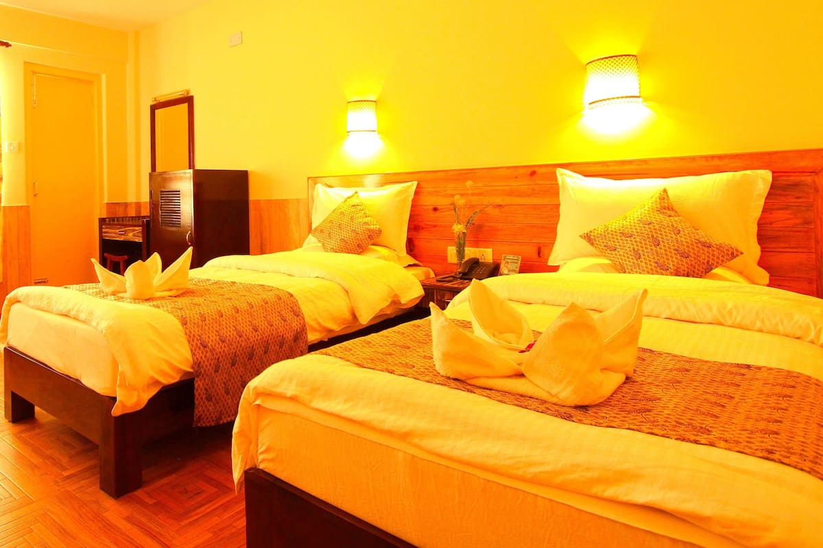 A hotel room with two beds, each with a wooden headboard, white linens, and decorative pillows. There are wall-mounted lamps and a small table with a telephone.