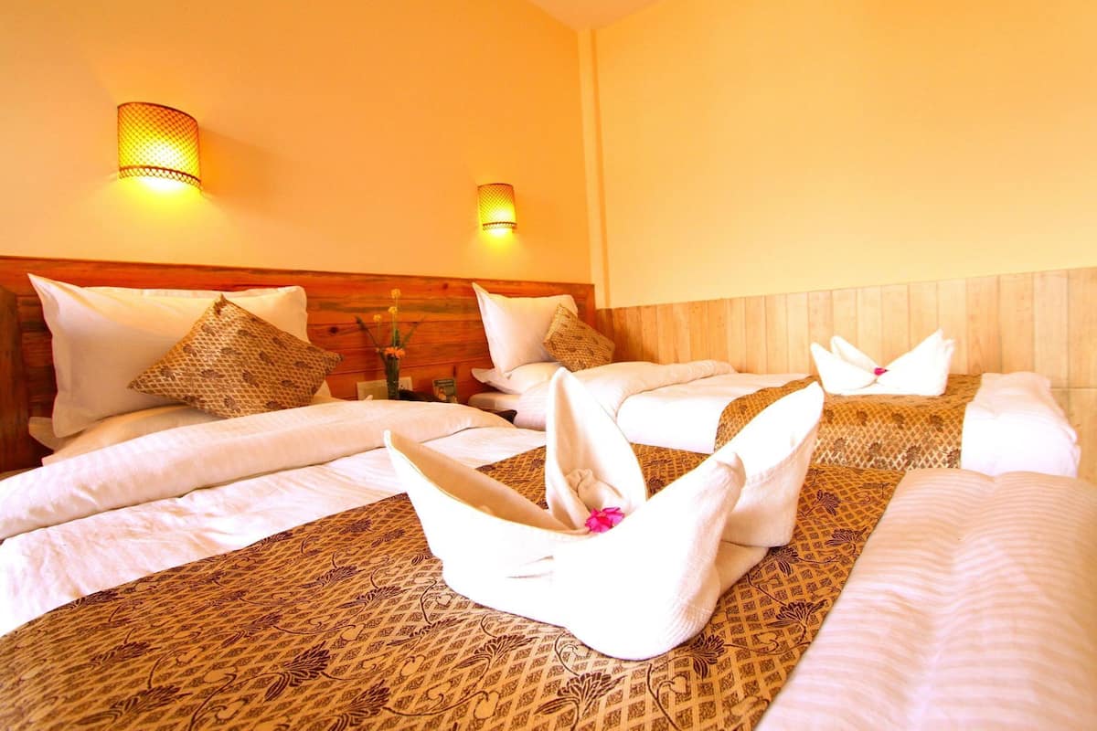 A hotel room with two beds, each with white linens and decorative towels. There are two wall-mounted lamps on the wall.