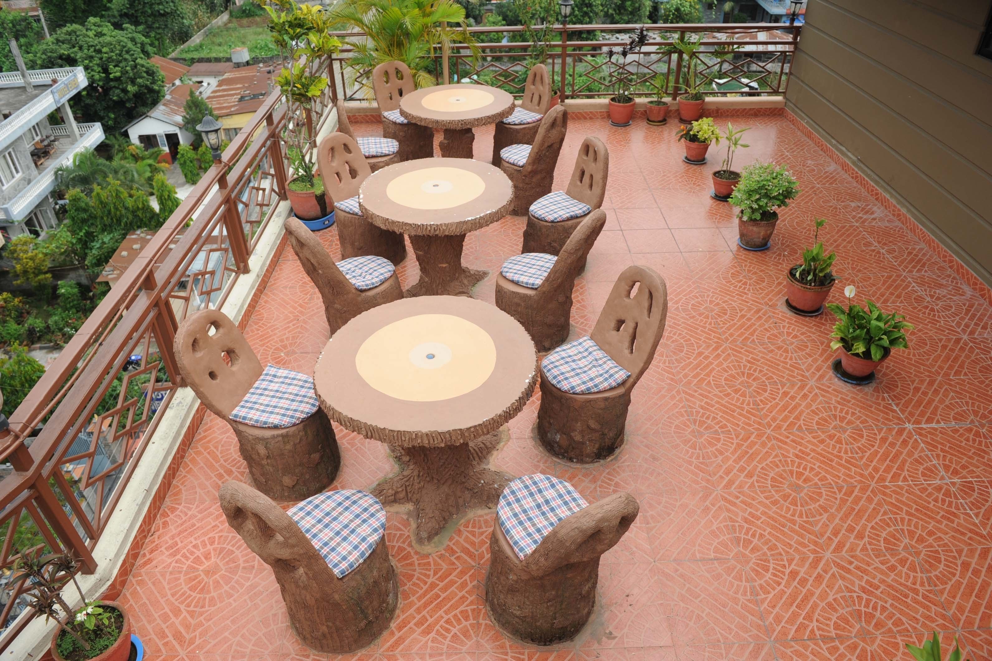 Una terraza con mesas y sillas de madera redondas, rodeada de plantas en macetas.