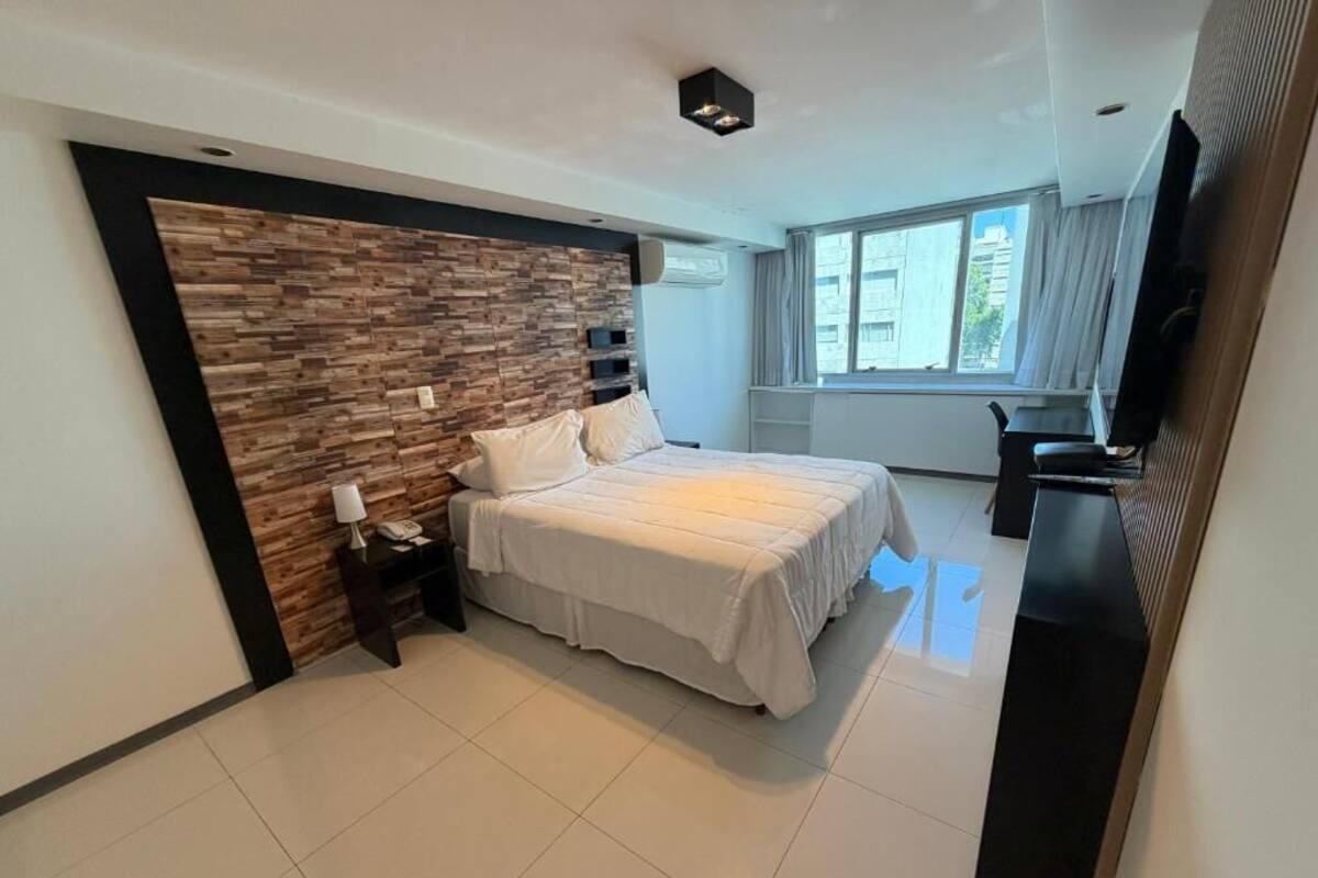 A modern bedroom with a large bed, a wooden accent wall, a bedside table with a lamp, and a TV on a stand.
