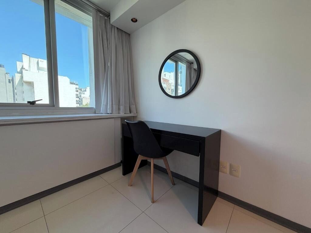 Una habitació amb escriptori, cadira, finestra amb cortines i un mirall rodó a la paret.