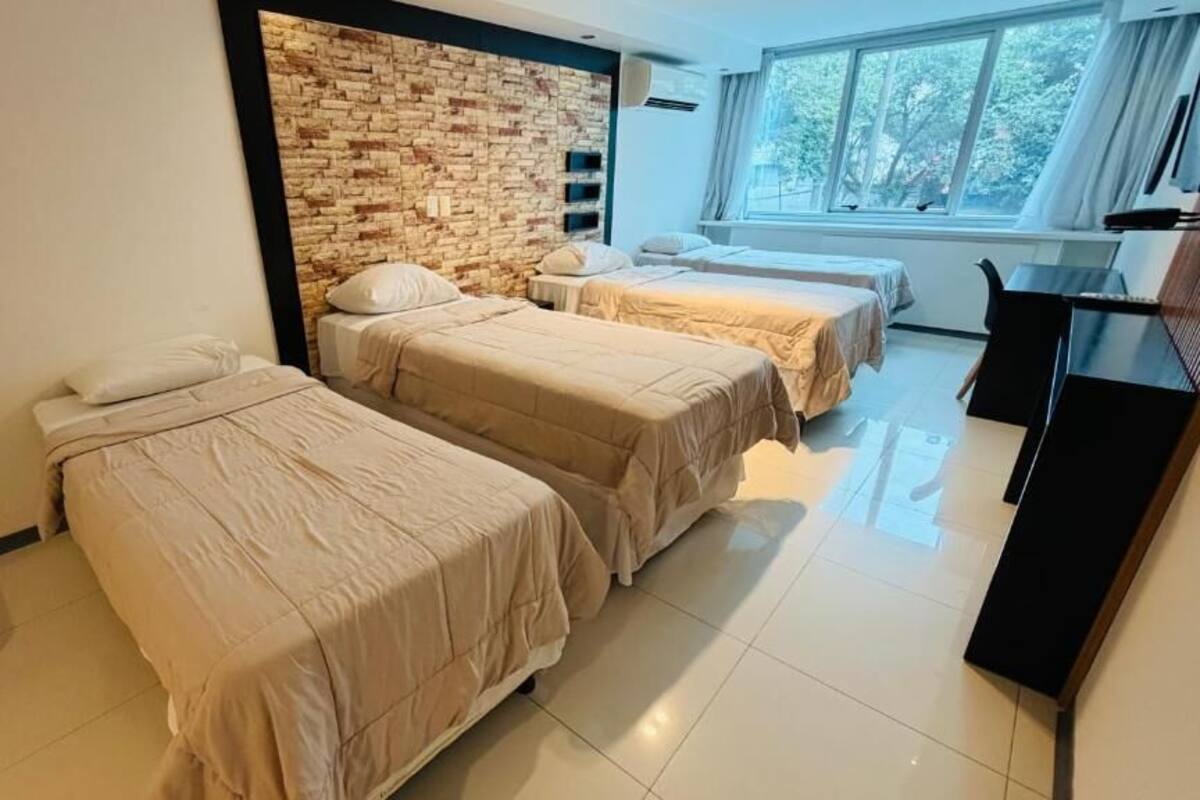 A hotel room with two beds, a brick accent wall, a desk, and a large window.