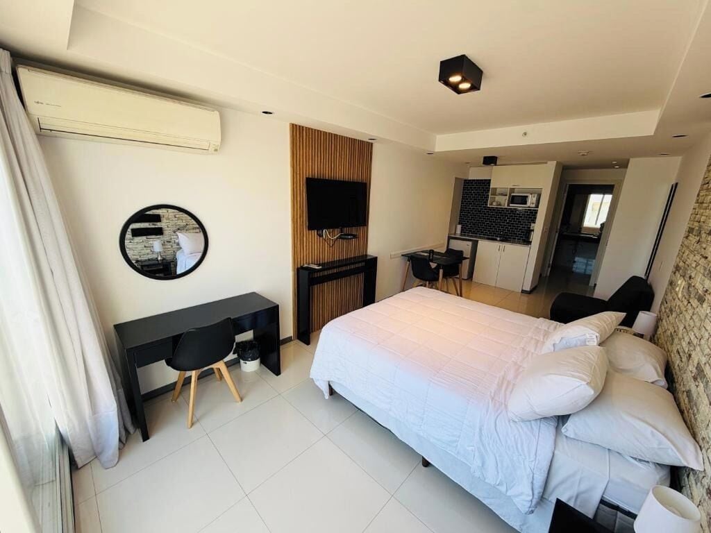 Habitación de hotel con cama, escritorio, silla, televisión y kitchenette.