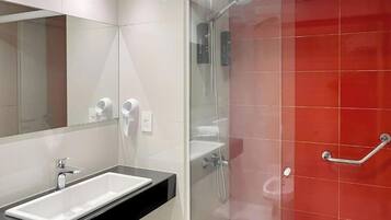 A modern bathroom with a glass shower enclosure, a white sink, and a handrail.