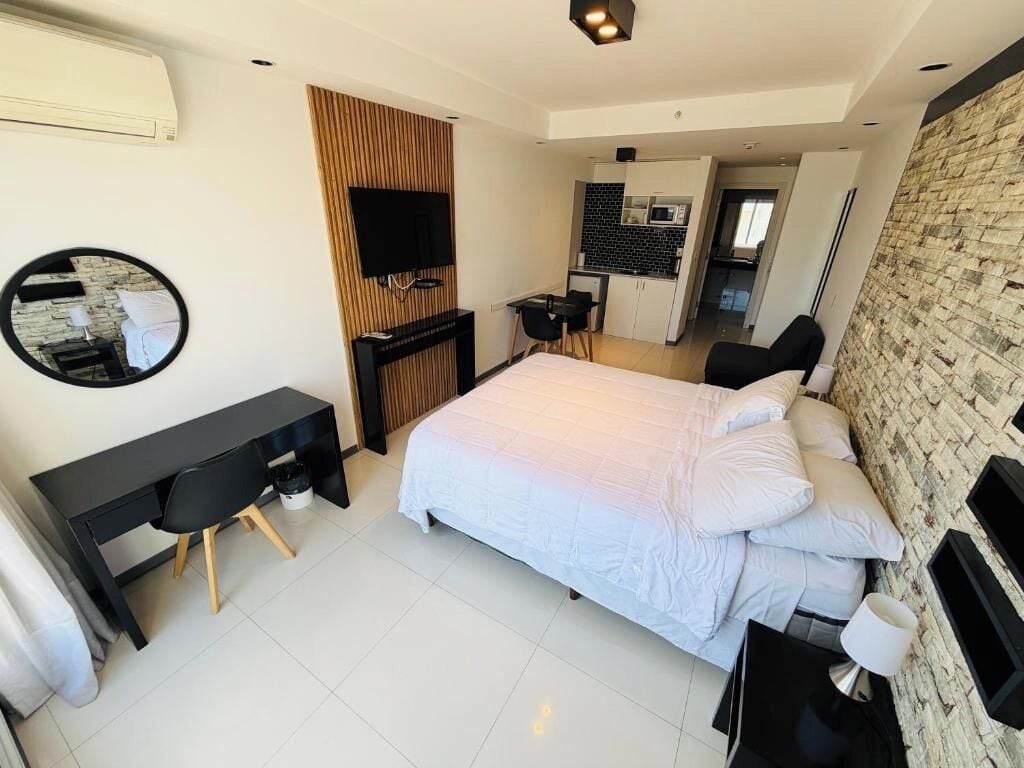 Un dormitorio moderno con cama, escritorio, televisor y kitchenette.