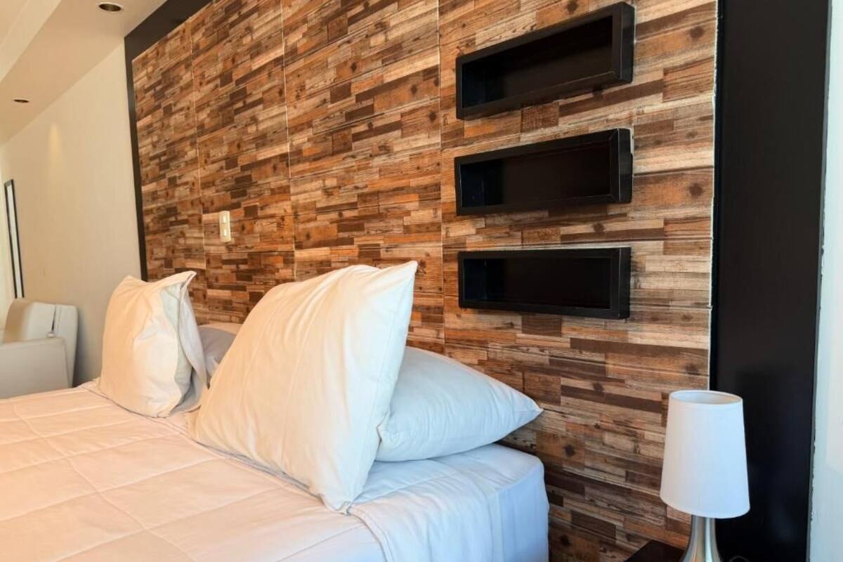 A bedroom with a wooden headboard, a bed with white bedding, and a bedside table with a lamp.