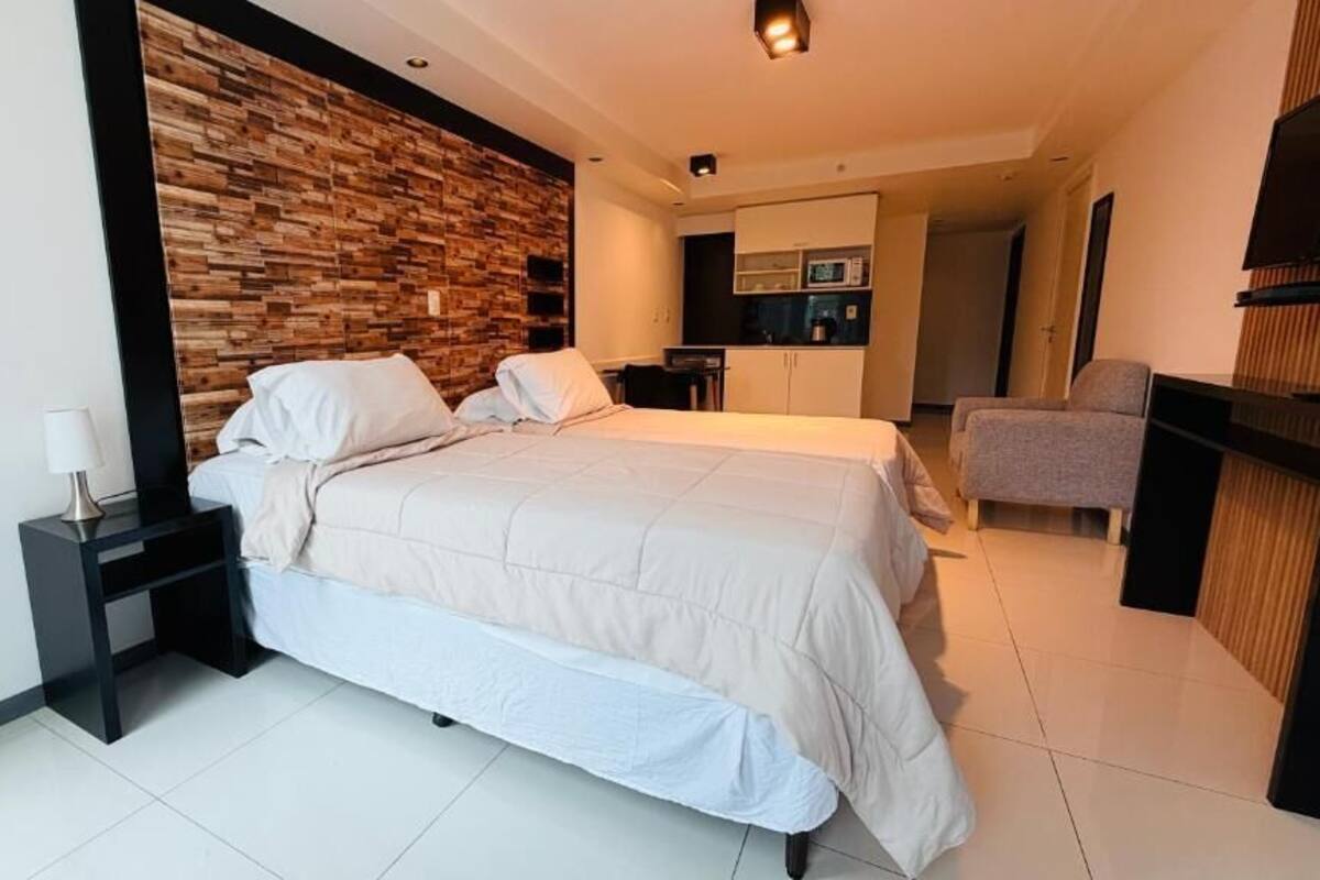 A modern hotel room with a large bed, a wooden accent wall, a small desk, and a seating area.