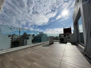 A rooftop terrace with a view of the city skyline, a glass railing, and a large window. - Gema Luxury Suites (Montevideo)