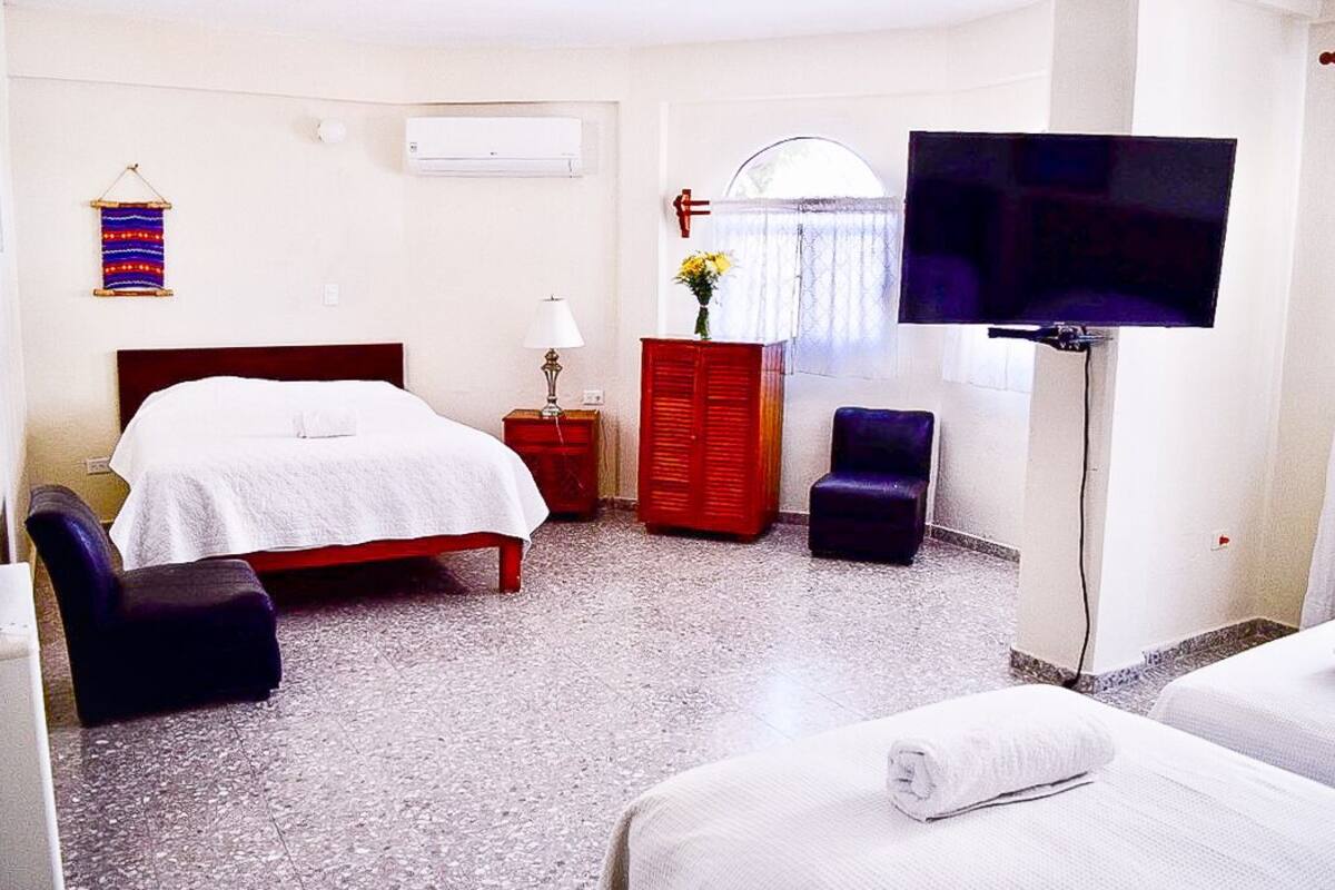 A hotel room with a bed, a TV, a chair, a dresser, and a small table with a lamp.